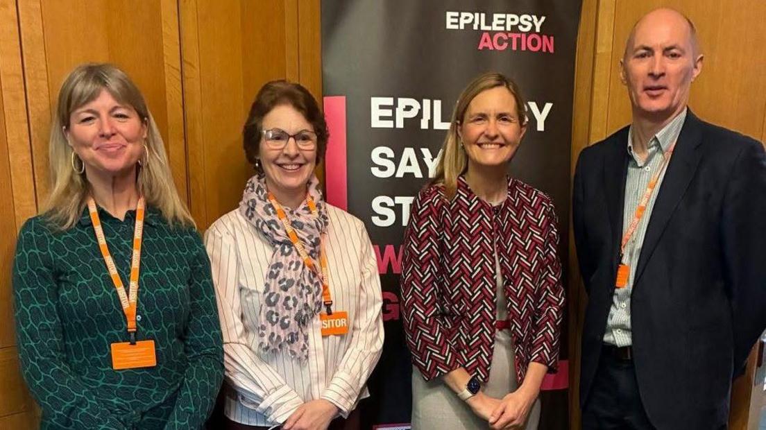 Four people stand smiling in front of an Epilepsy action board
