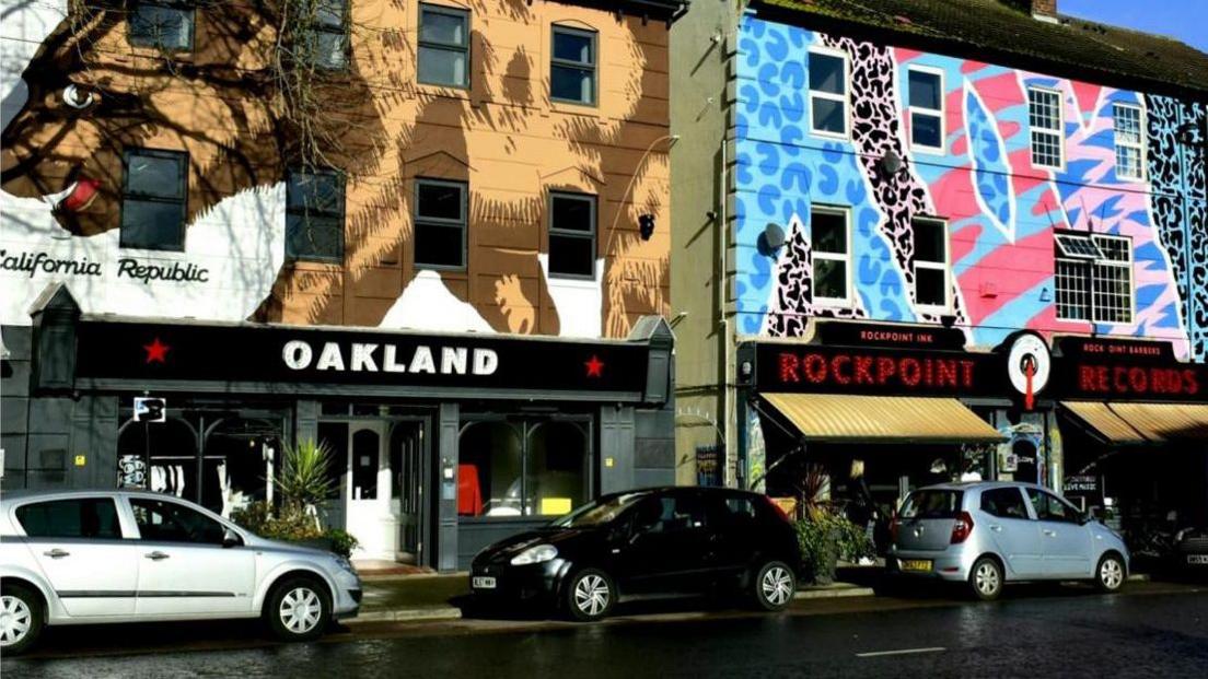 Exterior shots of the Oakland cafe and Rockpoint Records bar in New Brighton's Victoria Street. Both have large artworks painted on the front, including a large bear on the front of the Oakland.