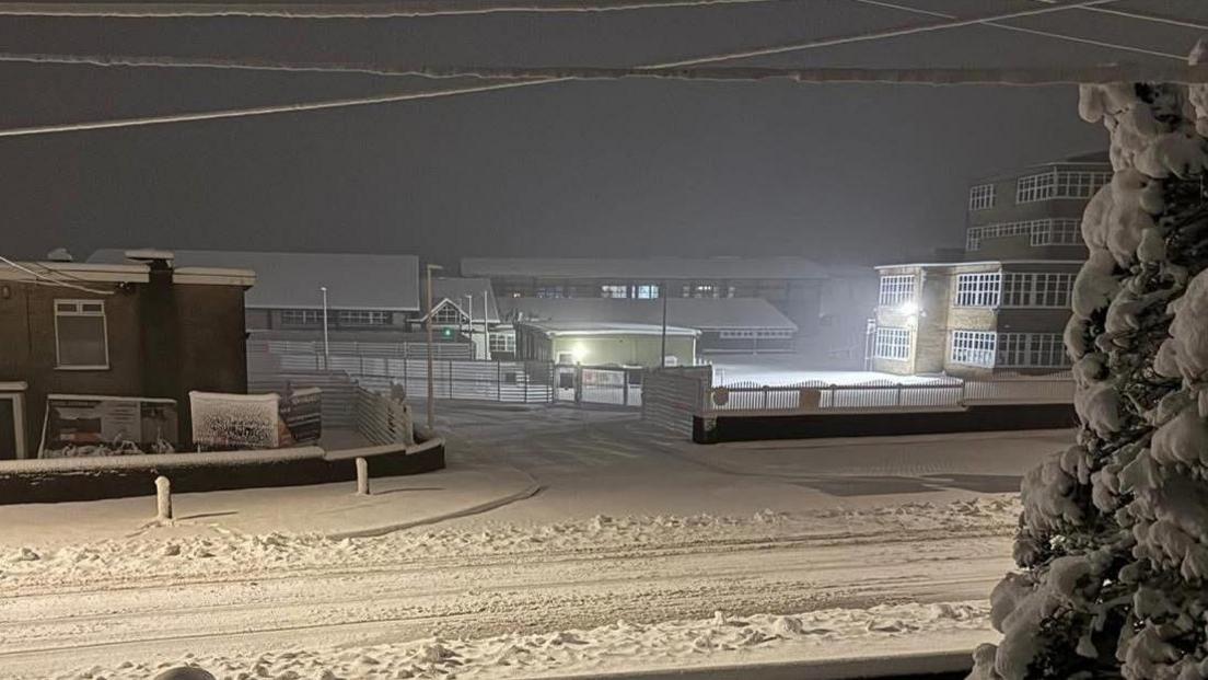 YSGOL BRO PRESELI seen from outside the school gates with the school yard and road covered in snow in the dark in the early morning. Street lights and outdoor lamps in the yard illuminate the buildings