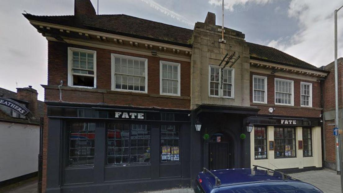 A brick building with the bottom half painted in anthracite with "Fate" written over the windows.