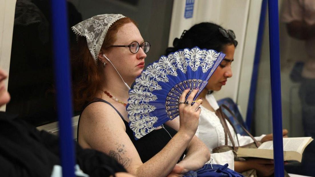 A woman with a bandana holding a blue fan sitting on the London underground