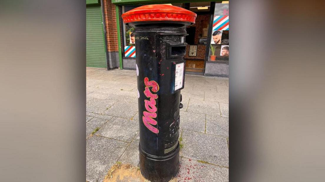 A Royal Mail postbox is painted black like a Mars bar. 