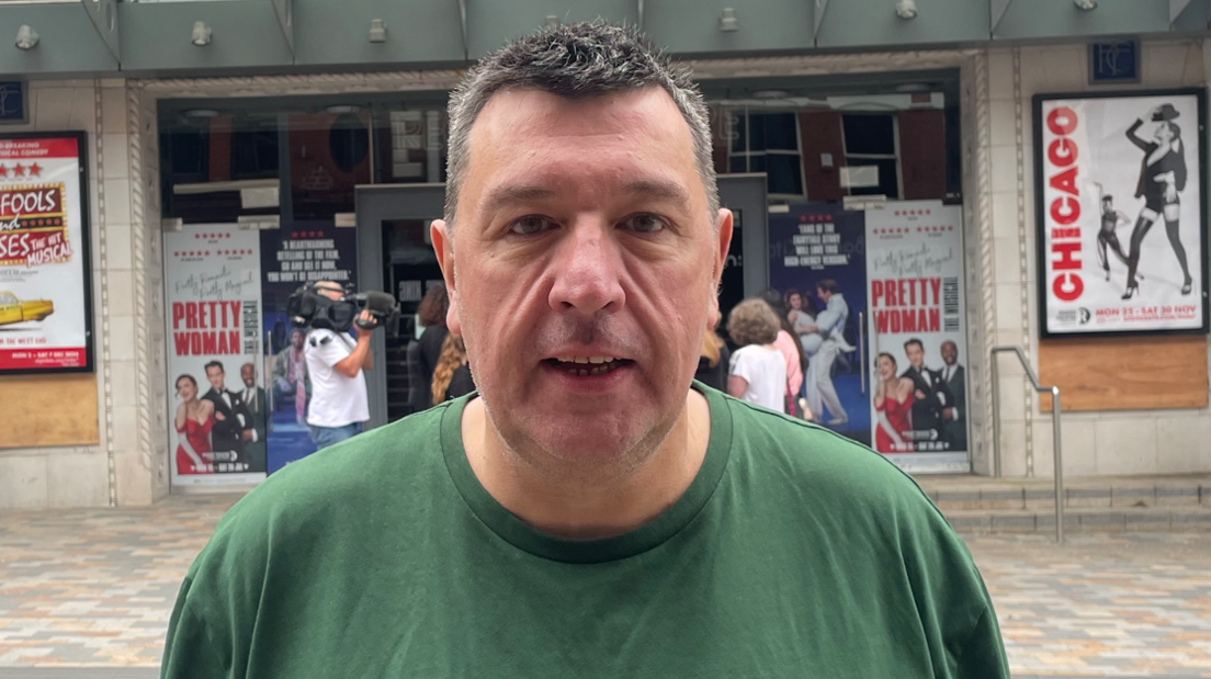 A middle-aged man in a green tshirt stood outside a theatre