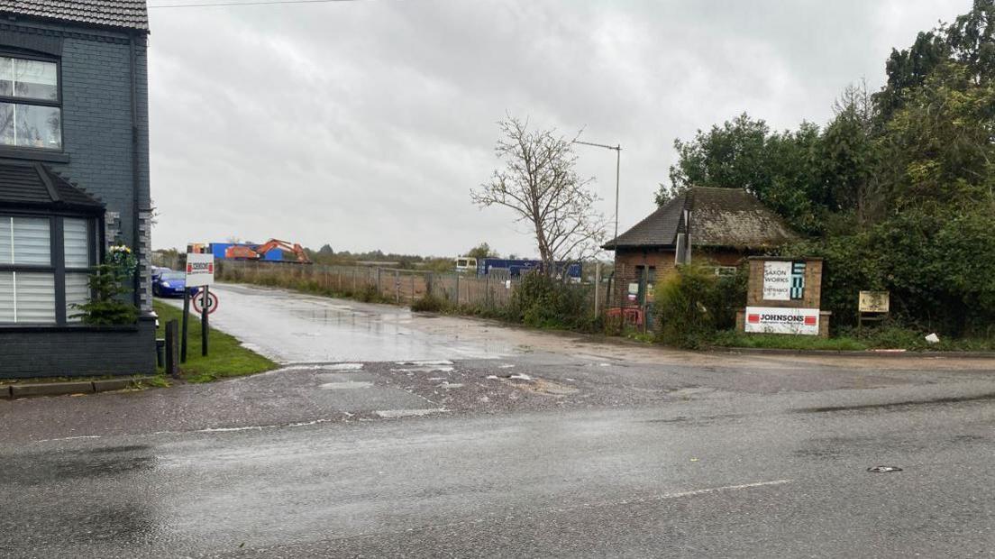 General view of the entrance to Saxon Pit. There are orange diggers in the far background and in the foreground signs which say "Saxon Works" and "Johnsons".