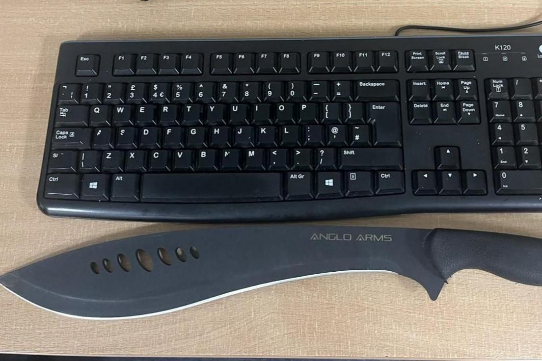 A machete knife placed below a computer keyboard.