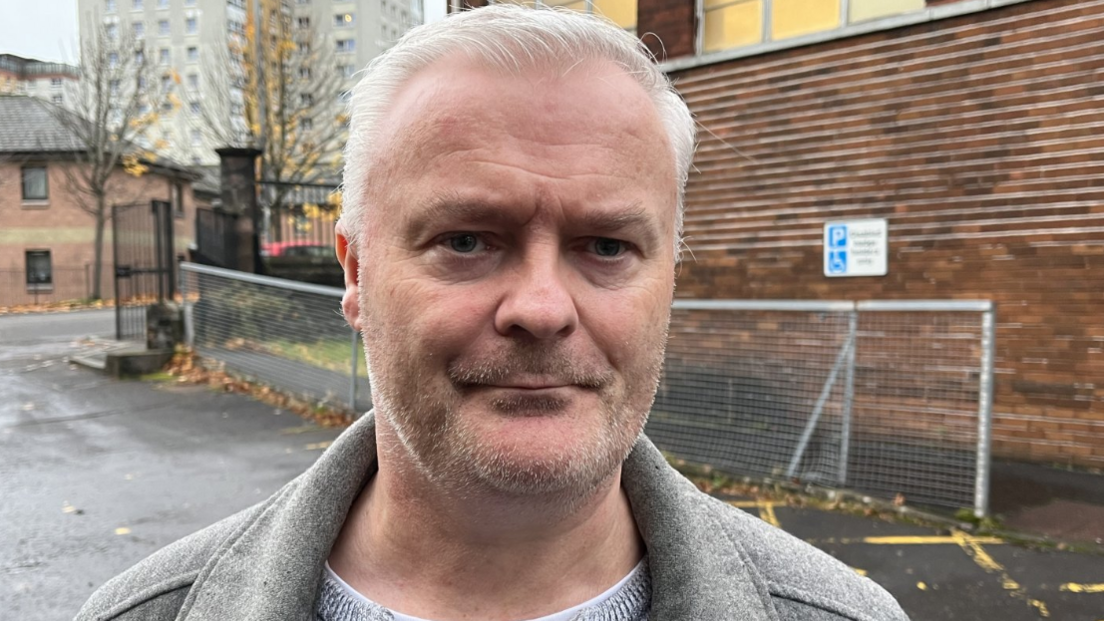 man with grey hair and stubble looks at camera