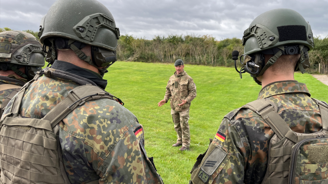 The backs of two German soldiers, with another soldier giving them instructions.