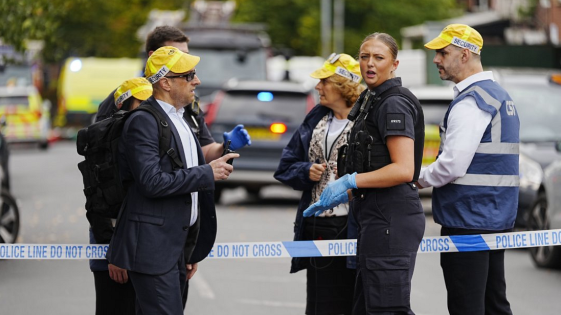 A police woman is shown along with security staff near a police cordon across a street