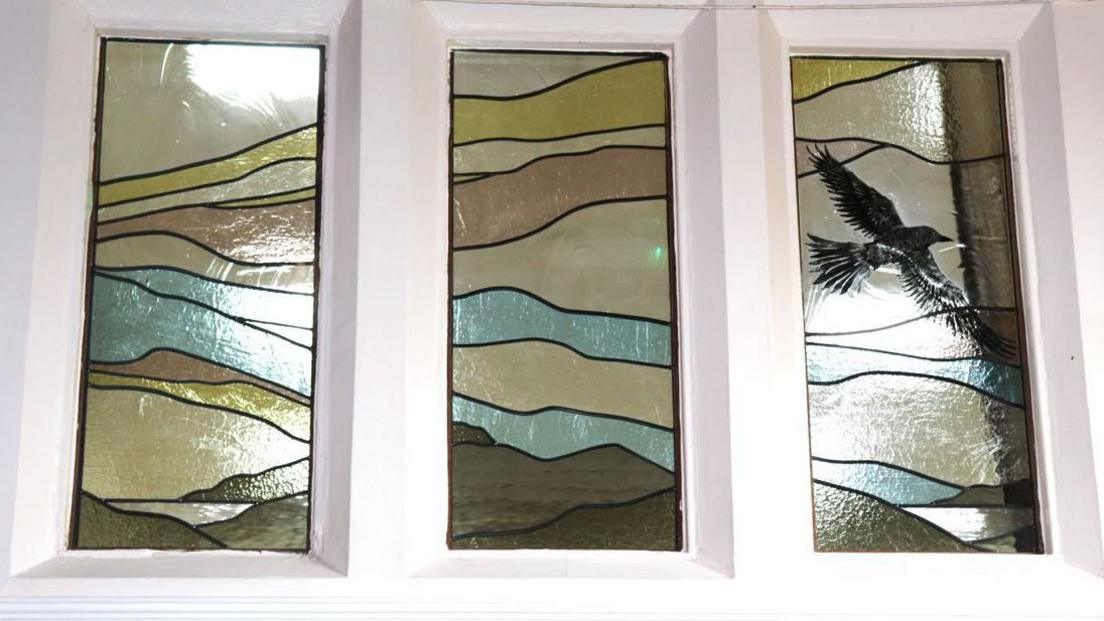 A close up view of three panels of stained glass showing a series of wavy lines and a black bird in flight