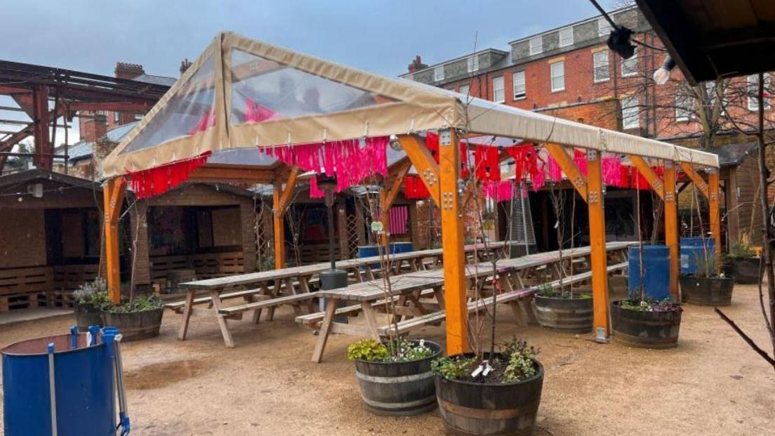 A tent shaped wooden structure with benches inside.