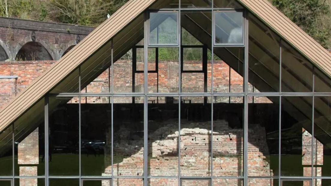 A large triangular structure with a large glass front over a brick structure