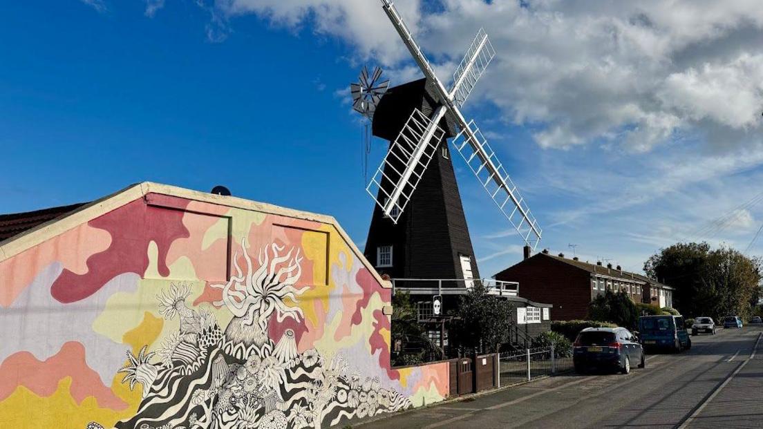 A street view of a wooden-framed windmill standing over a colourful building.