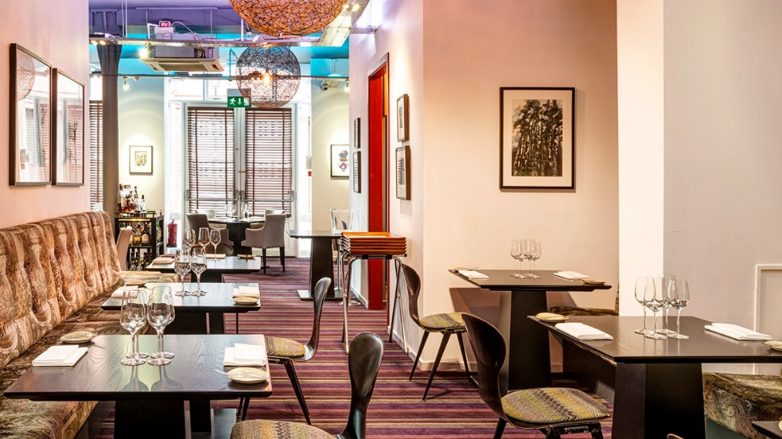 The interior of a carpeted restaurant with chairs and tables set with with wine glasses and napkins. 