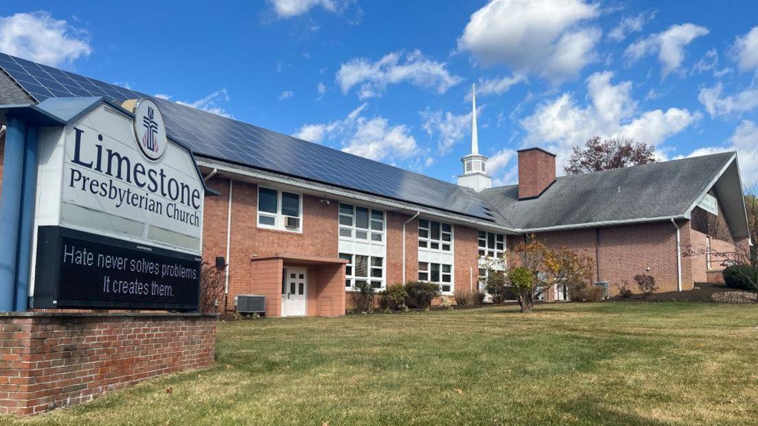 Limestone Presbyterian Church has a red brick exterior with white windows and a black roof. In front of the building is a blue and white sign with the churches' name on it. Beneath that is the electronic sign which contains a message.