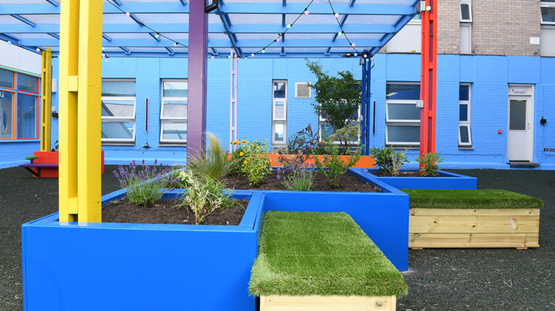The colourful garden at the hospital. Planters are painted blue as are the walls. A hard floor has been put down with seating and new windows.