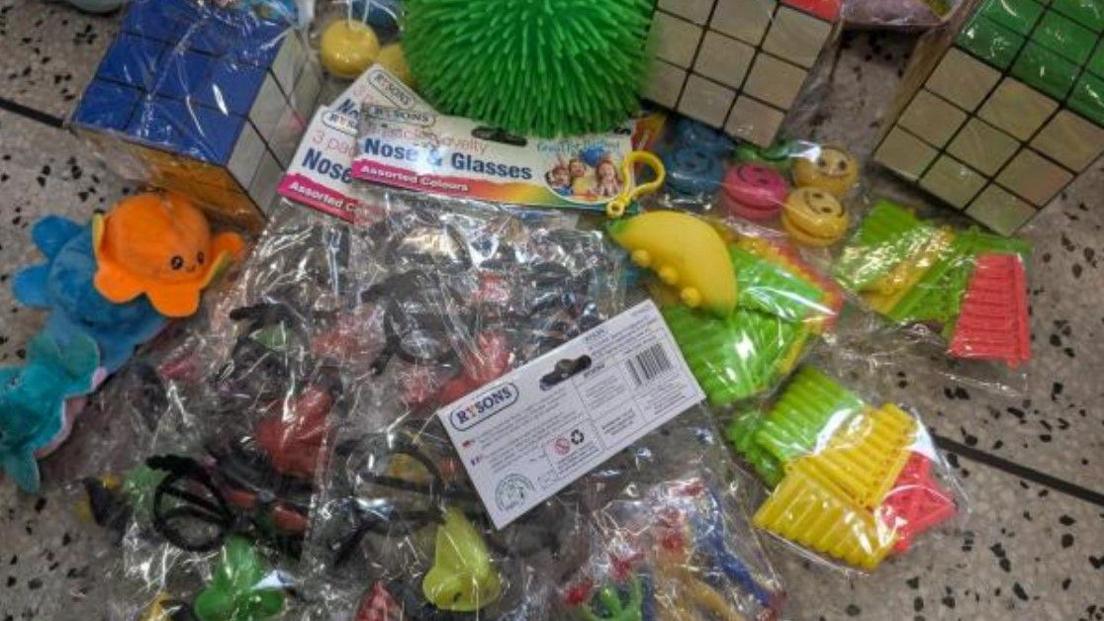 Accessories of different colours are on the floor , loose and in plastic bags. At least one bag is labelled Nose & Glasses.