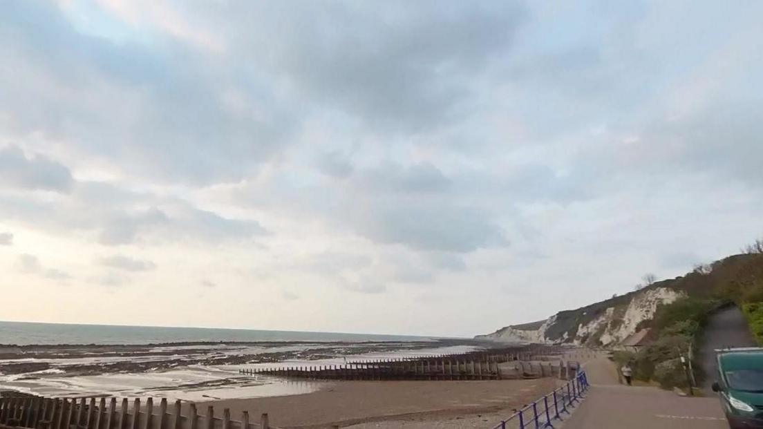 Eastbourne seafront is seen with cliffs in the background and the tide leaving pools on the beach