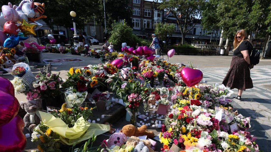 A woman looks at floral tributes and stuffed teddy bears in memory of Elsie Dot Stancombe, Bebe King and Alice Dasilva Aguiar