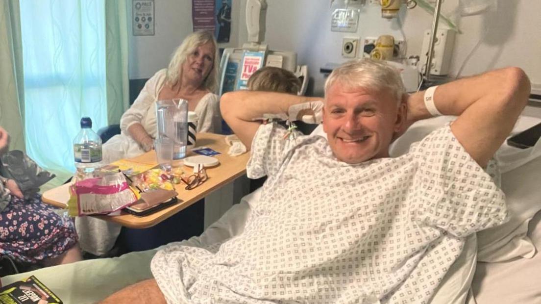 Tony Pilkington lies in a hospital bed with his family after receiving treatment