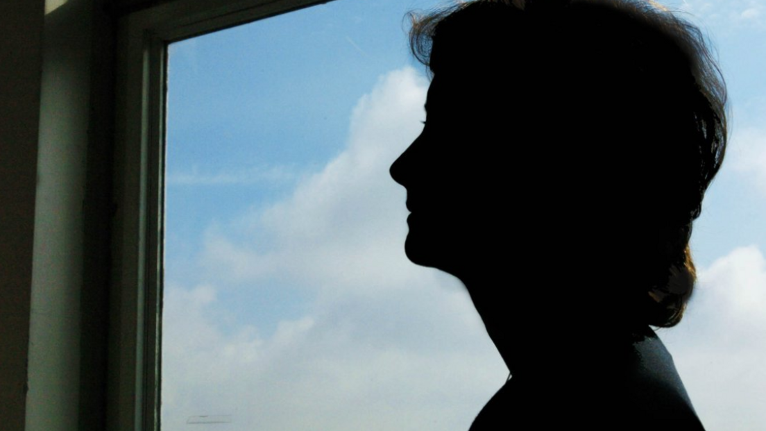 A silhouette of a woman standing by a window that shows blue sky and clouds