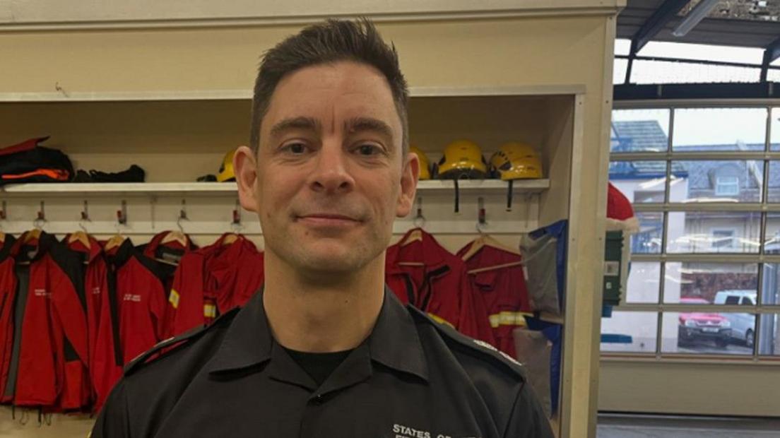 John wearing a blue States of Jersey uniform and standing in the fire station