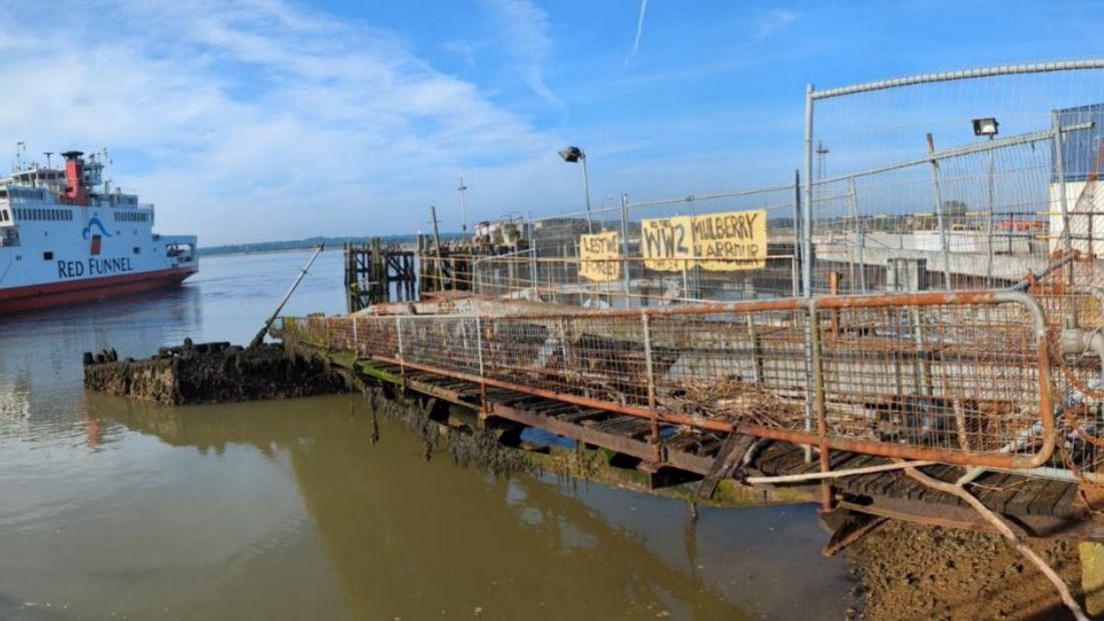 The Whale roadway section and buffer pontoon of a Mulberry Harbour to the east of Royal Pier at Town Quay in Southampton. A Red Funnel Ferry is passing by. It is a clear day.