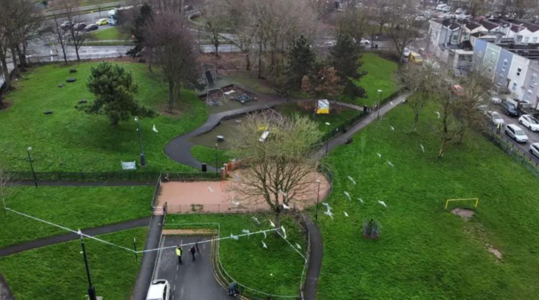 Aerial view of park, with police cordon in place. Several police officers are stood near police tape.