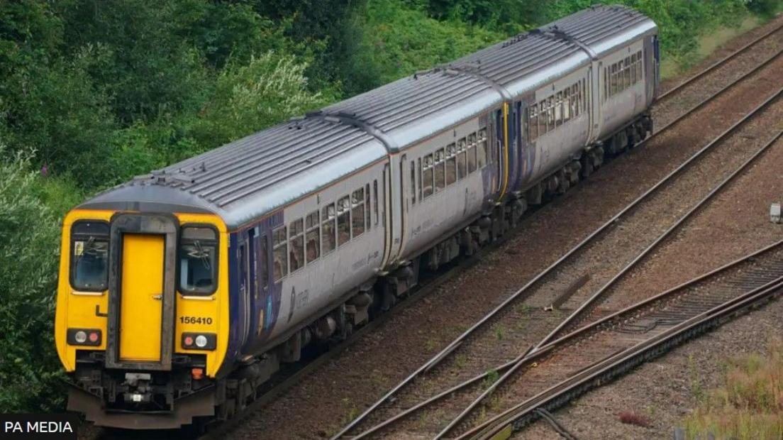 A grey, blue and yellow Northern train, with four carriages.