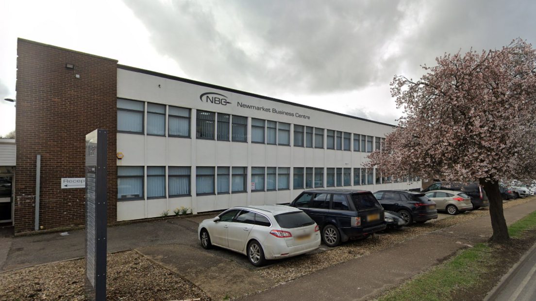 The exterior of the Newmarket Business Centre. The building has a white front and is lined with windows across two storeys. Cars are parked outside.
