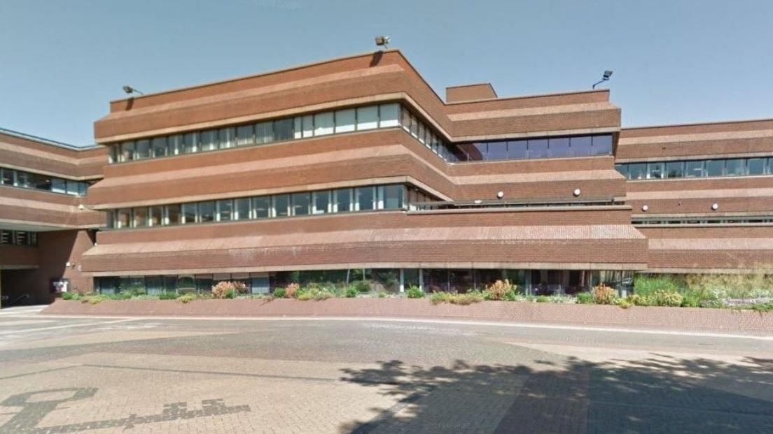 A three-tier building is in the background, with a pedestrianised area in front of it.