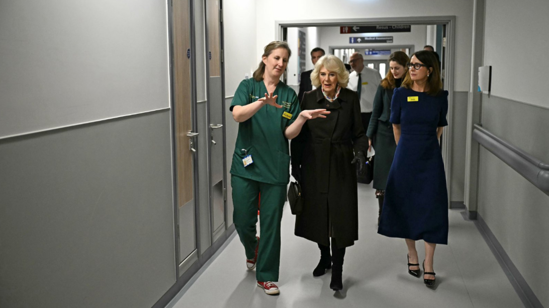 The Queen is shown around the new emergency department by a member of staff with various others following behind 