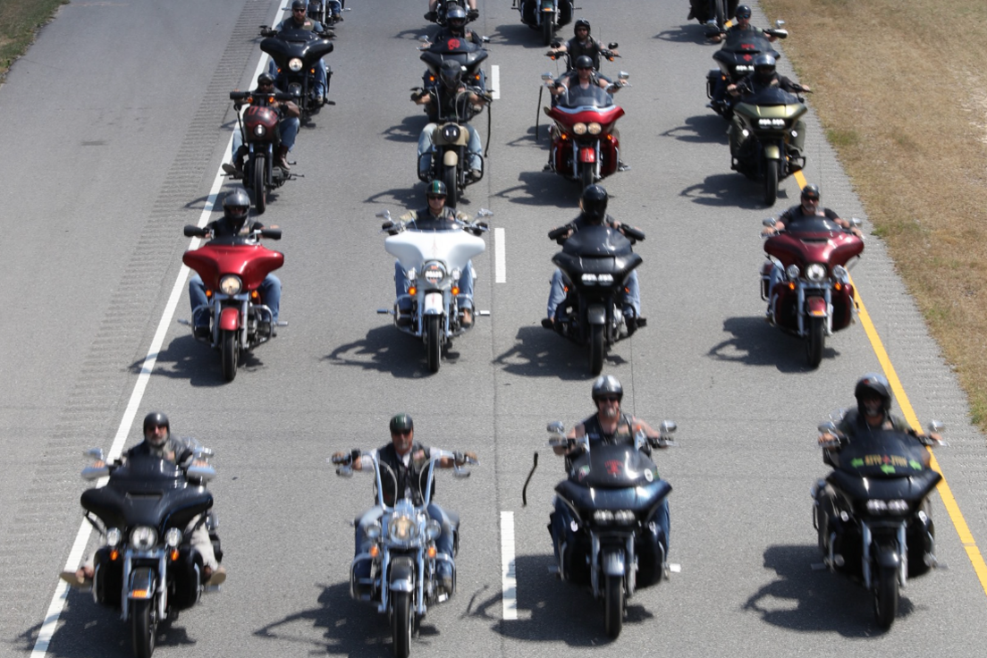 About a dozen bikers from the Infidels MC gang seen riding in formation, some with chopper-style handlebars in chrome, photographed from a high vantage point 