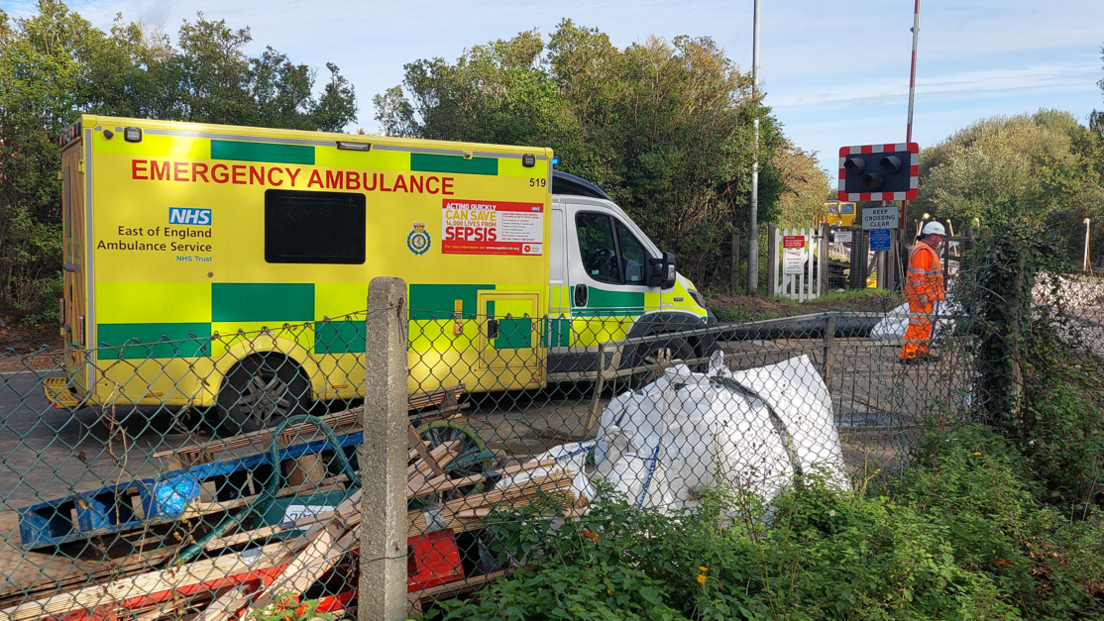 An ambulance parked at a level crossing. A worker in a hard hat is standing in front of it.