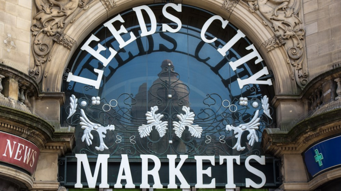 Leeds City Markets sign which is large white lettering and some foliage, set in a stone archway over the door to the market