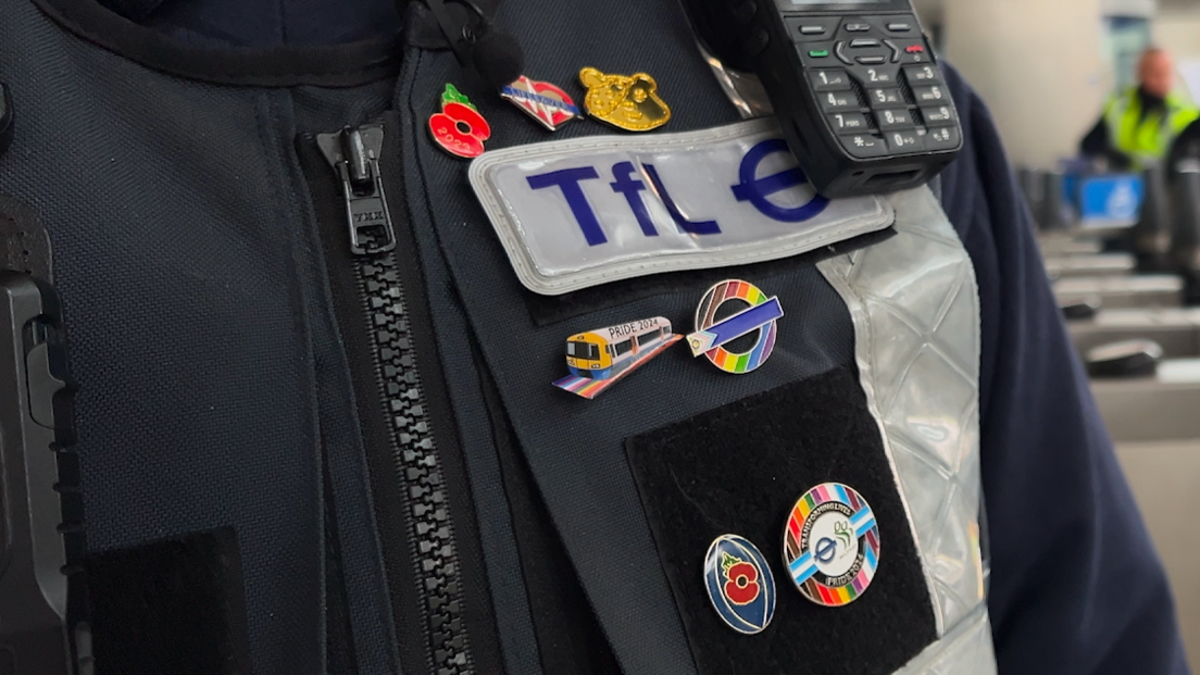 TfL officer's uniform - a zip-up top with a walkytalky and a number of pin badges to demonstrate inclusivity - Pride rainbows, a bear and poppies