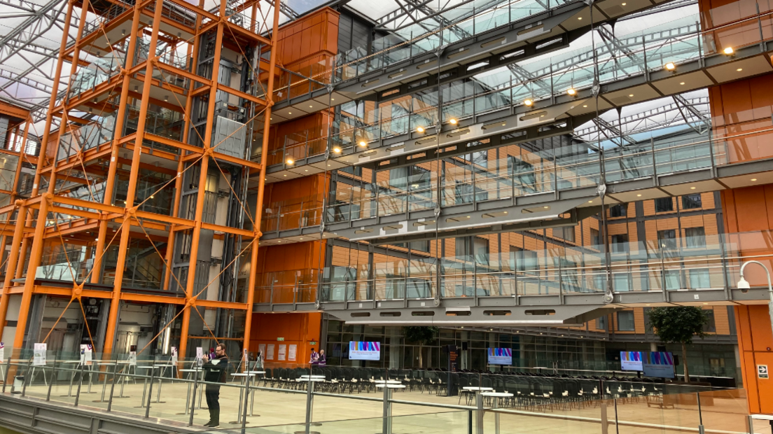 A man standing in front of a five-storey glass-fronted building with an orange support structure