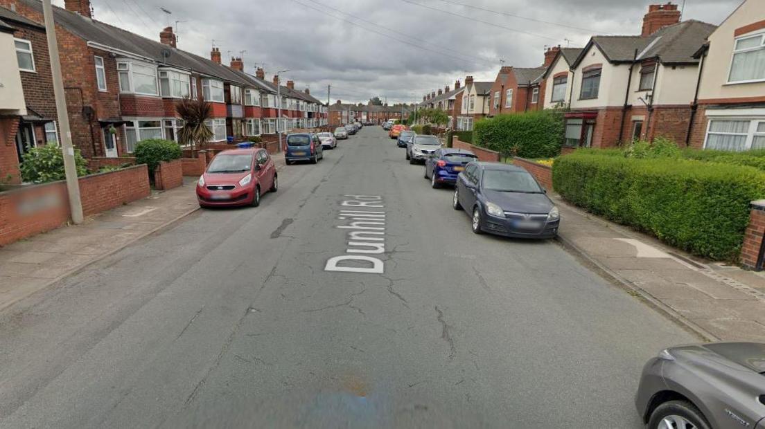 Dunhill Road, with terraced housing down both sides and cars parked on both sides of the road