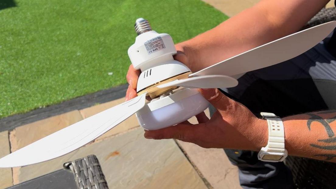 A man is holding a screw fit ceiling fan light. It has cream wings and a cream base. The light is covered with white plastic.