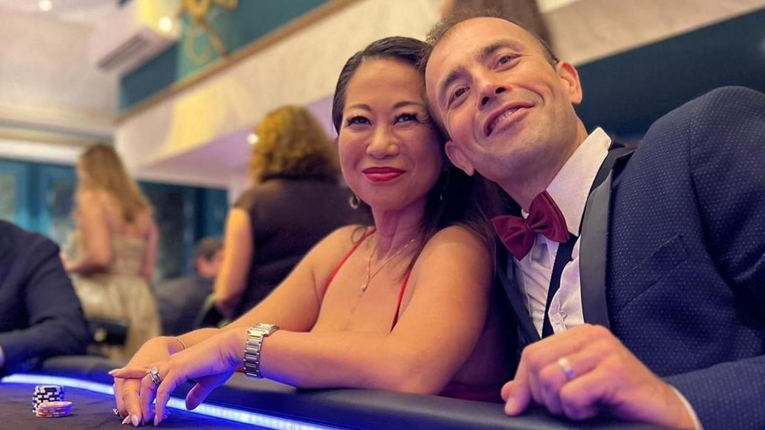 Line Young Peteri at a poker table with her husband. He wears a suit and bow tie, and she wears a dress.