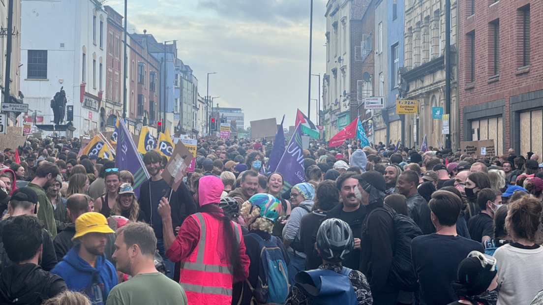 A large crowd of people standing together, some holding flags