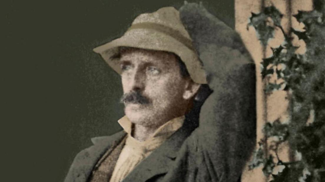 An old image of a man with a moustache in a hat next to what looks like a holly plant