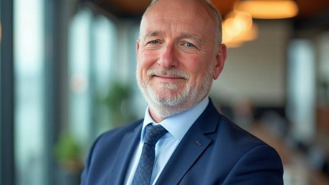 Steve Robertson, a man with a close grey beard and blue eyes, wearing a blue suit and tie. He is looking into the camera with a slight smile
