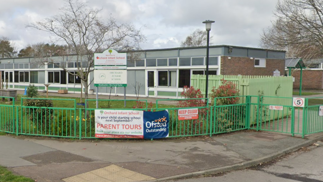 The outside of Orchard Junior School - a single storey building surrounded by a green mental fence.