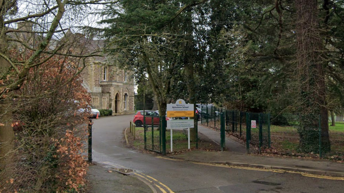 A Google Streetview of a school, taken from the road. A Victorian building sits at the end of a tree-lined driveway. A sign at the gate reads: "Welcome to Aylestone School".