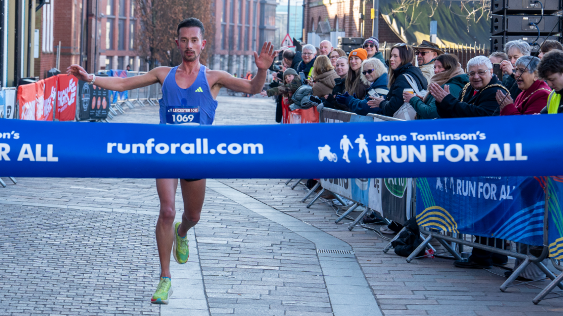 Runner in blue with green trainers lifting his arms as he's about to cross the finish line  