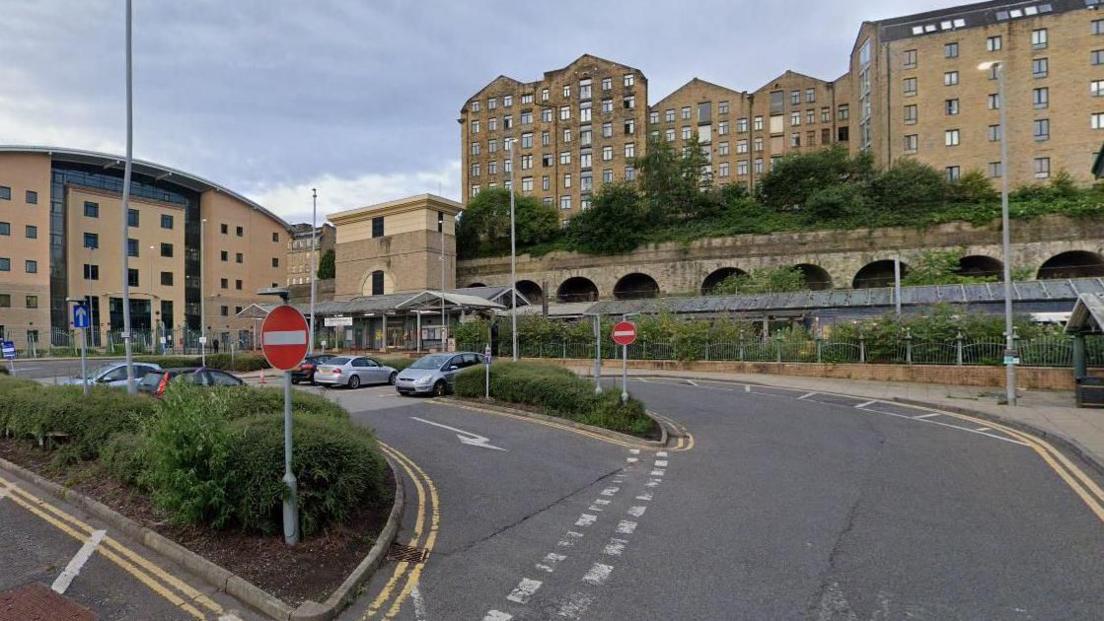 A car park outside a railway station with railway tunnels and buildings in the background