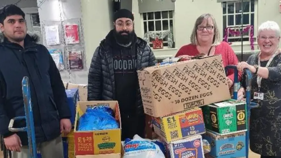 A trolley with boxes of food being handed over by two supermarket staff and Kelly Brown and Trisha Bennett 