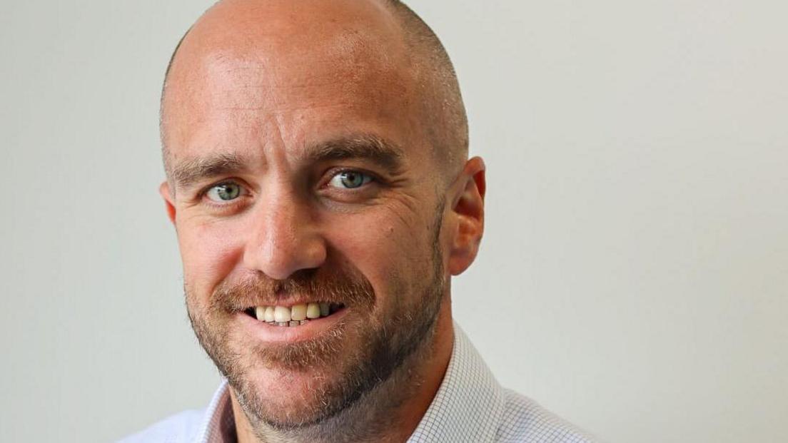 A bearded balding man with a blue checked shirt.