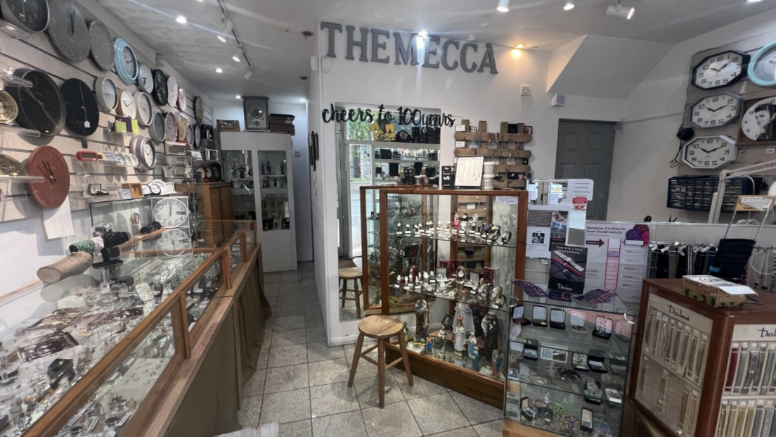 Shop with white walls tiled floor, wooden panelled jewellery stands and clocks on walls