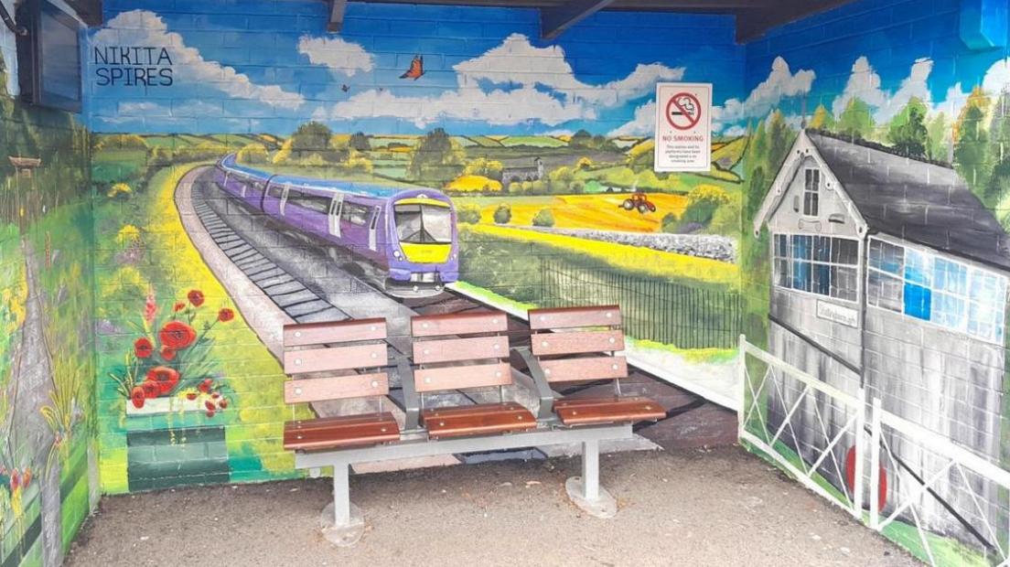 Brightly-coloured mural of a modern train on a railway line flanked by flowers and trees, with a signal box in the foreground.